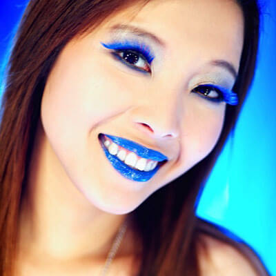 woman with blue lipstick and blue eyelashes smiling at the camera