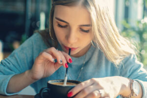 Young woman sipping a dark beverage through a straw, highlighting strategies for enjoying holiday drinks while protecting dental health.