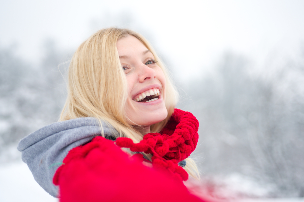 Smiling woman in a red scarf enjoying winter scenery, emphasizing dental health and cosmetic dentistry.