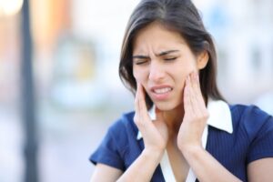 Woman experiencing jaw pain, holding her face, illustrating the importance of sports guards in preventing TMJ injuries and protecting overall dental health.