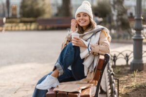 Young woman enjoying a warm drink while sitting on a park bench in winter attire, highlighting the importance of warm beverages for managing tooth sensitivity in cold weather.