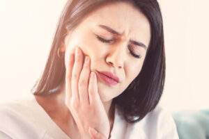 Woman experiencing dental pain, holding her jaw, indicating potential issues with fillings or crowns, related to oral health concerns.