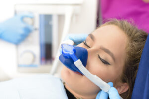Patient receiving nitrous oxide sedation during dental treatment, wearing a nasal mask for relaxation, with dental equipment visible in the background.