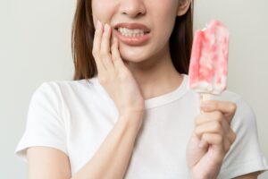 Woman holding a popsicle while grimacing in pain, indicating tooth sensitivity or discomfort, relevant to discussions on toothaches and the importance of dental care.