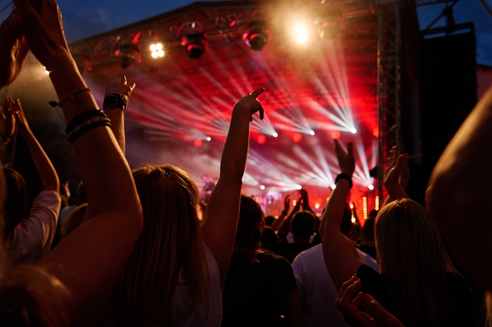 Crowd at outdoor music festival with bright stage lights and raised hands